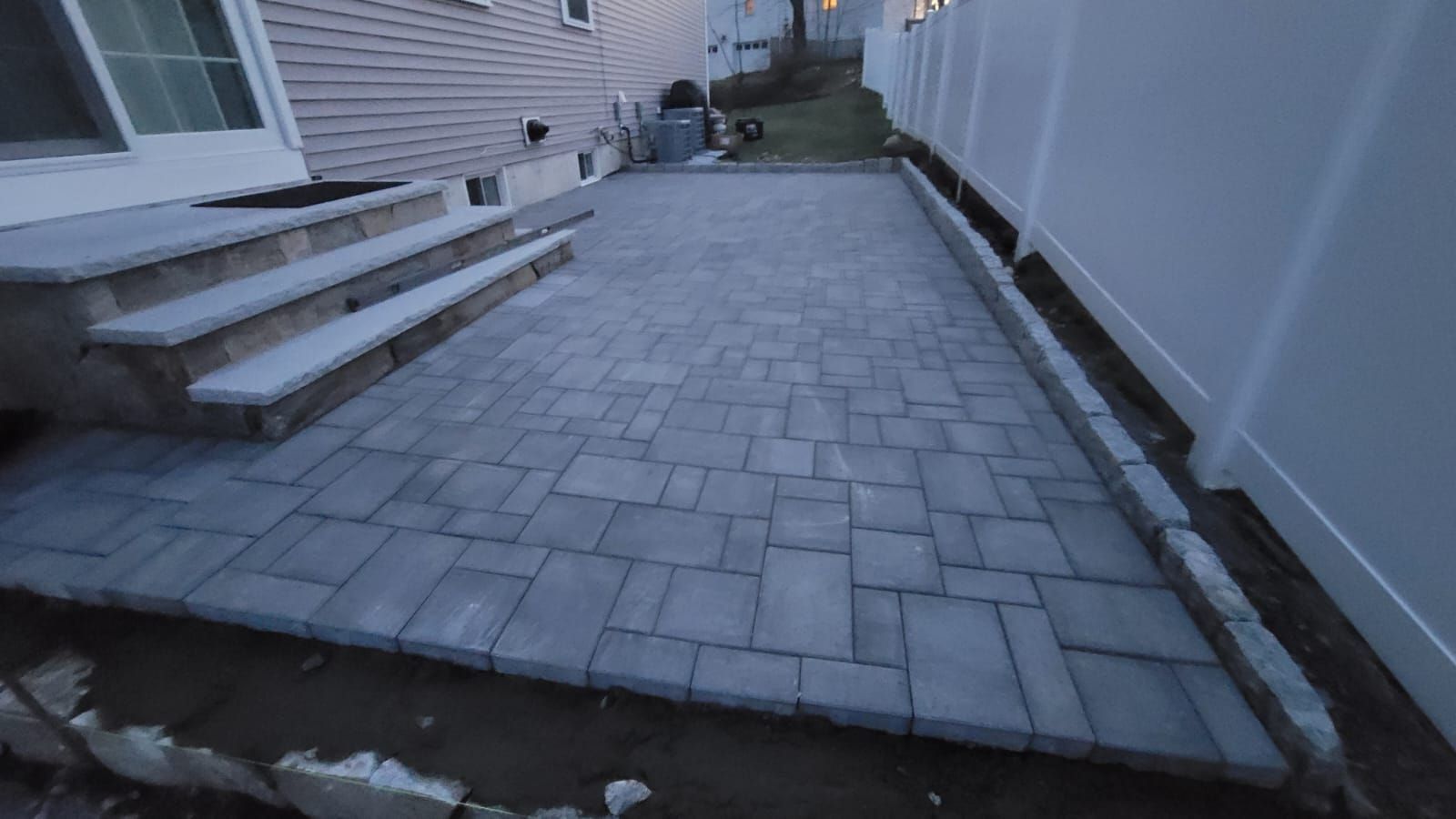 A patio with steps and a white fence in front of a house.
