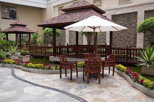 A table and chairs under an umbrella in front of a gazebo.