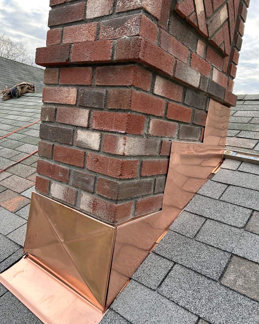 A brick chimney on top of a roof with a copper gutter.