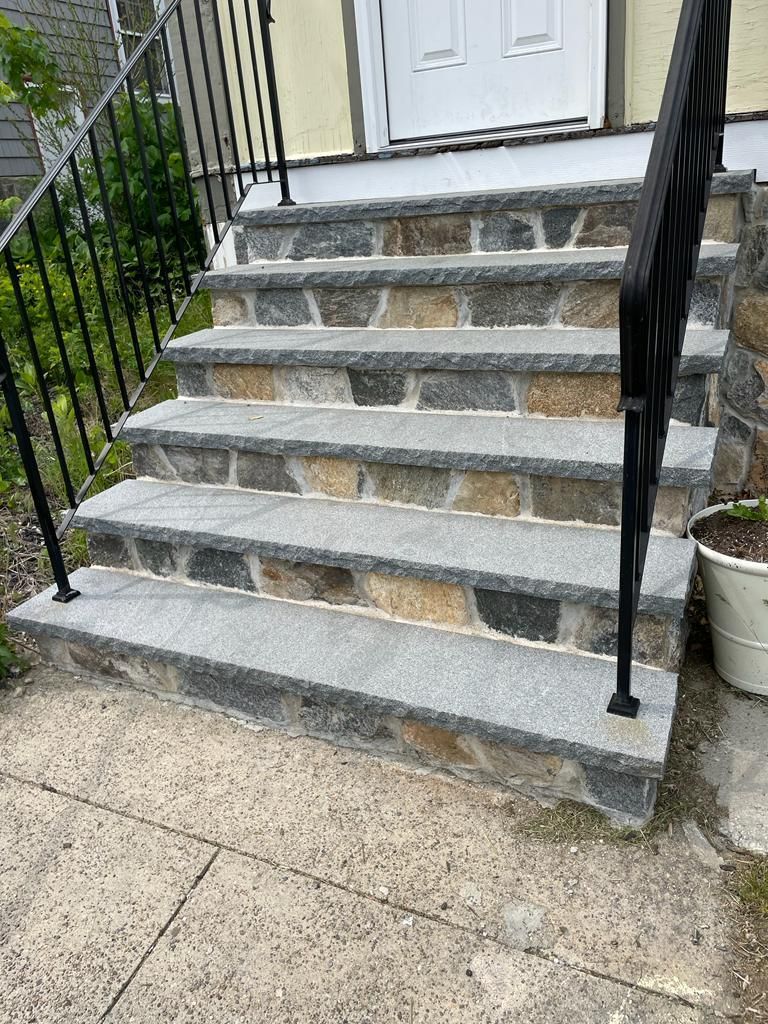 A set of stone stairs leading up to a house with a metal railing.