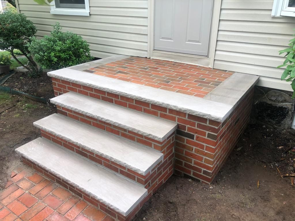 A brick porch with steps leading up to the front door of a house.