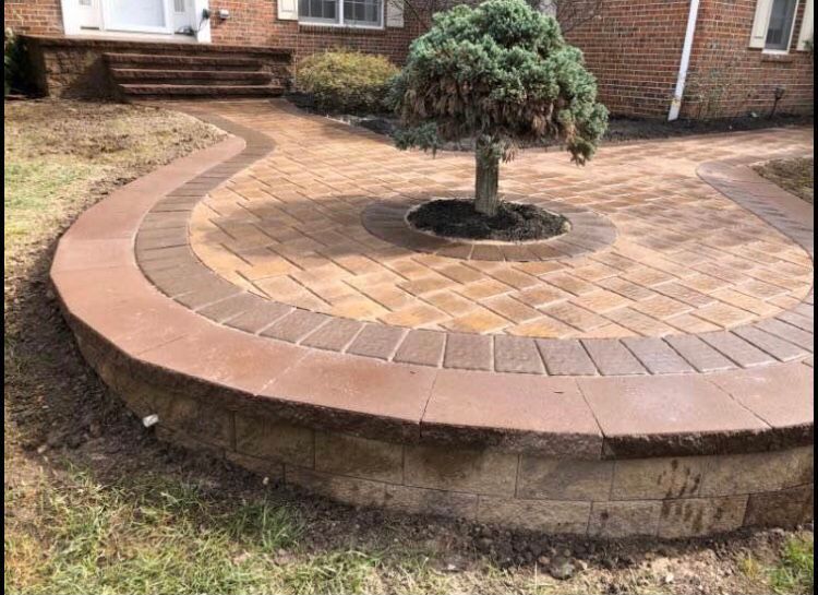 Brick patio with a curved border, small tree, and steps leading to a house.