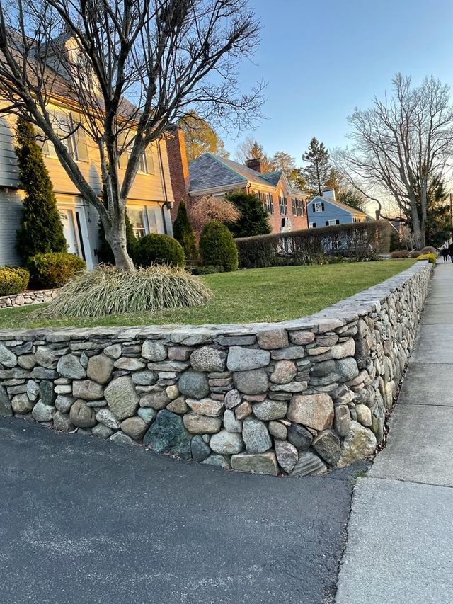 A stone wall surrounds a lush green lawn in front of a house.