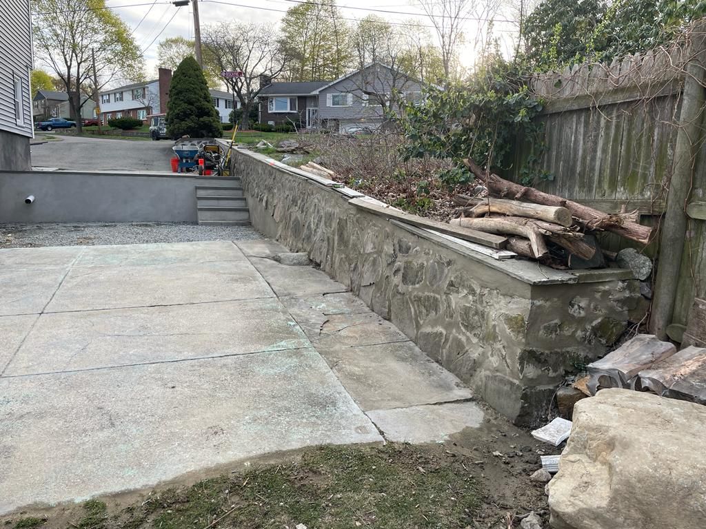 A pile of logs is sitting next to a stone wall in a backyard.