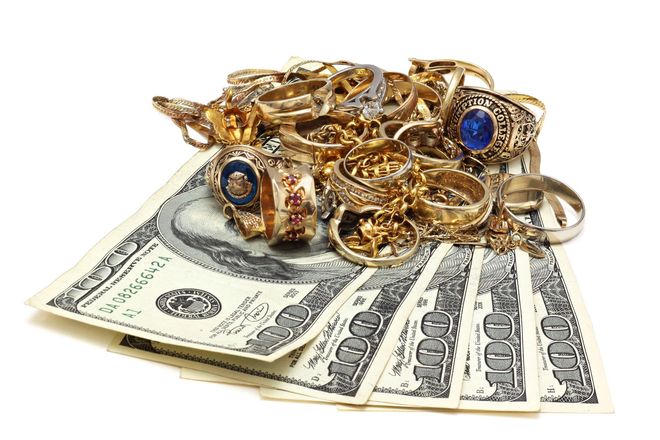 Pile of gold rings and jewelry atop several hundred-dollar bills.
