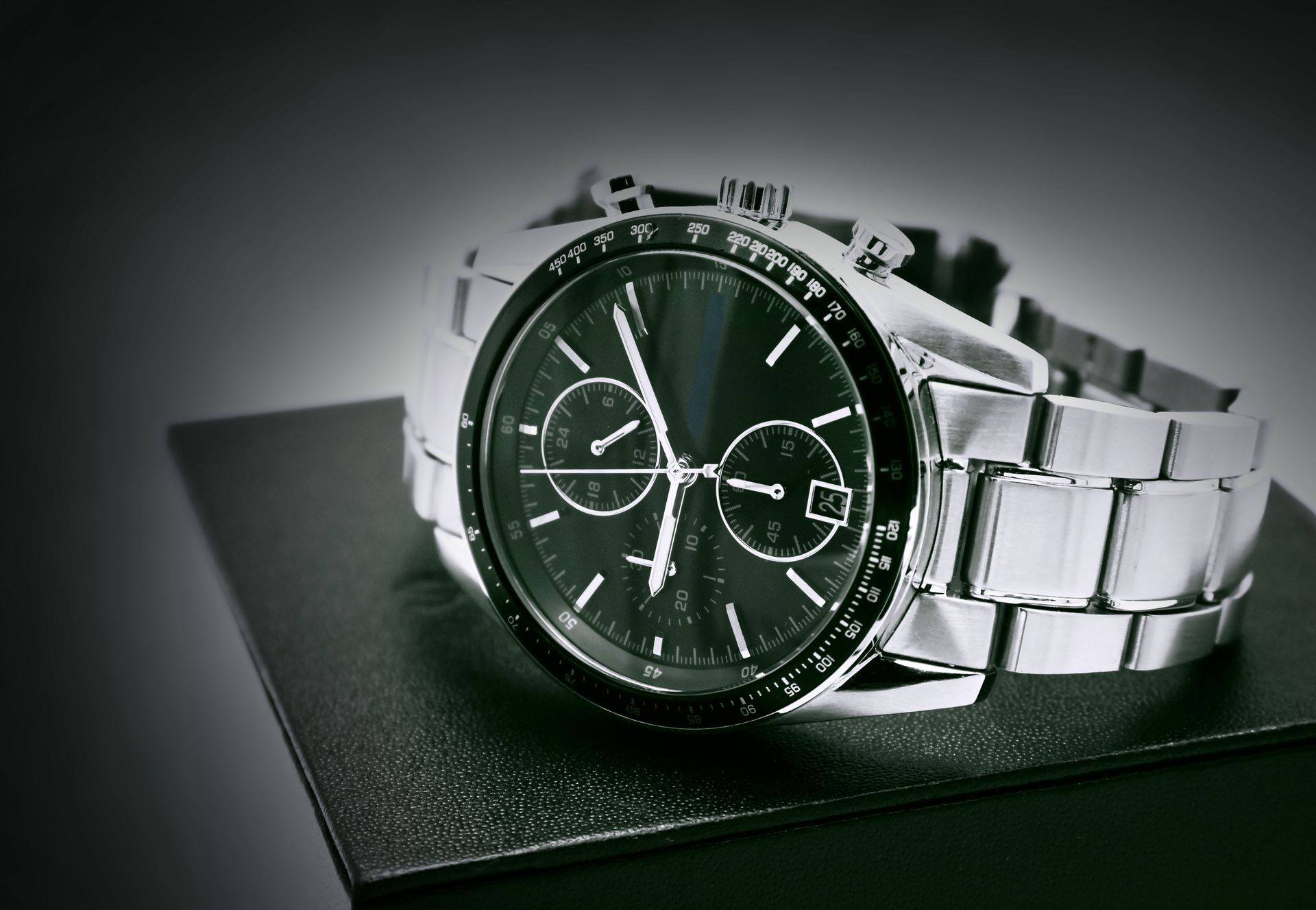 Silver wristwatch on a black box, with a dark face and detailed dial.