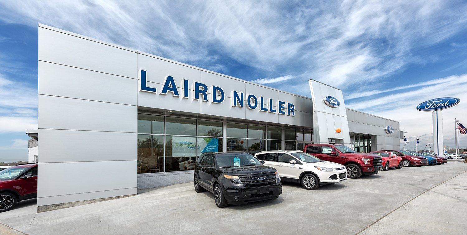 A row of cars are parked in front of a ford dealership.