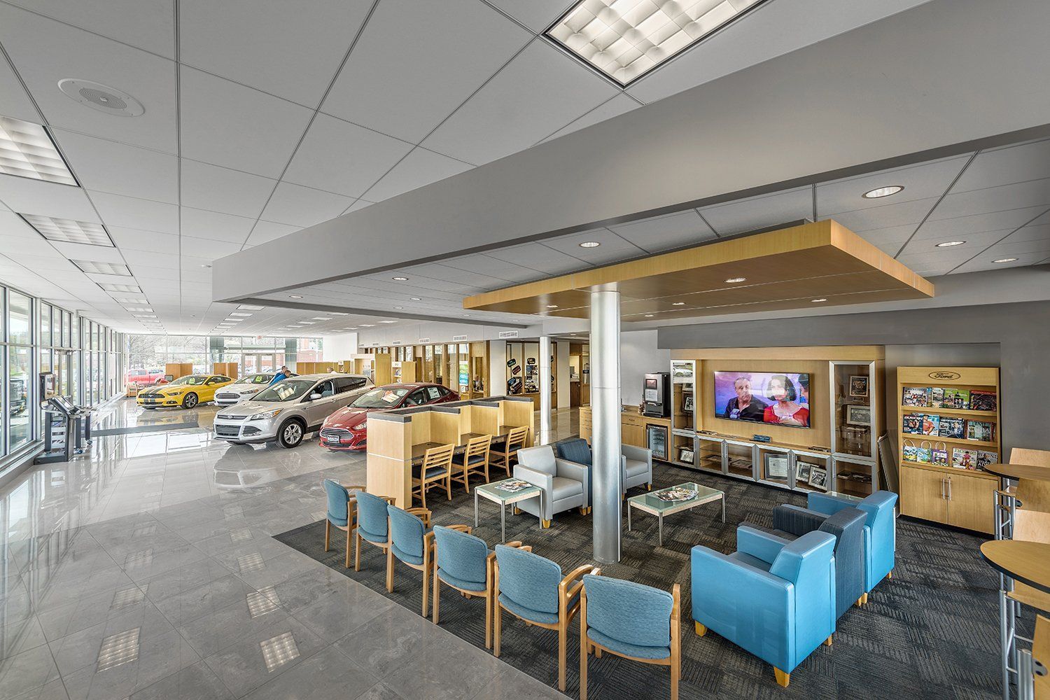 A waiting area in a car dealership with chairs , tables and a television.