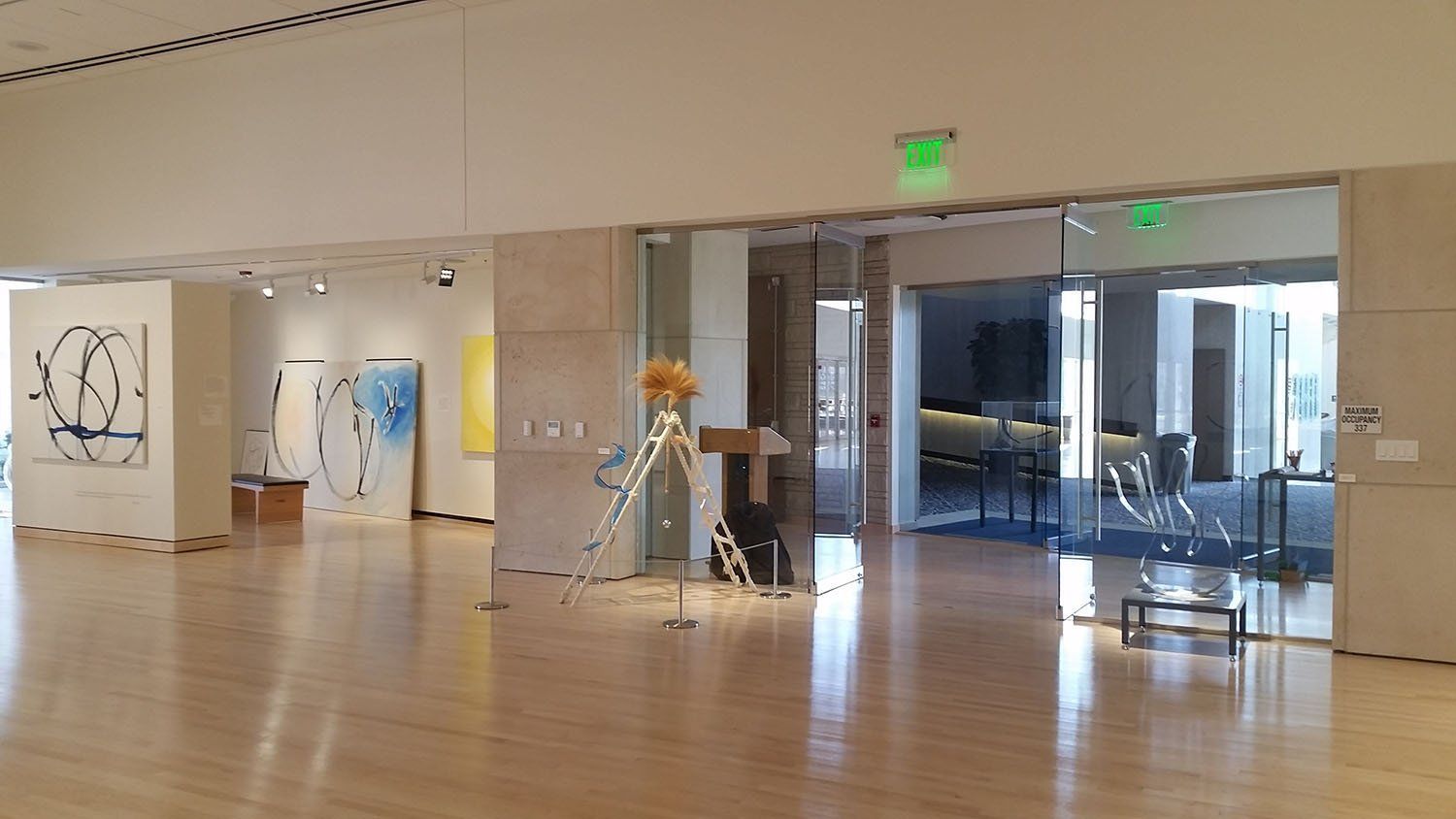 A large empty room with a lot of paintings on the walls and a green exit sign.