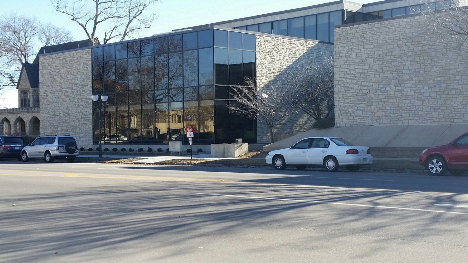A white car is parked in front of a large building