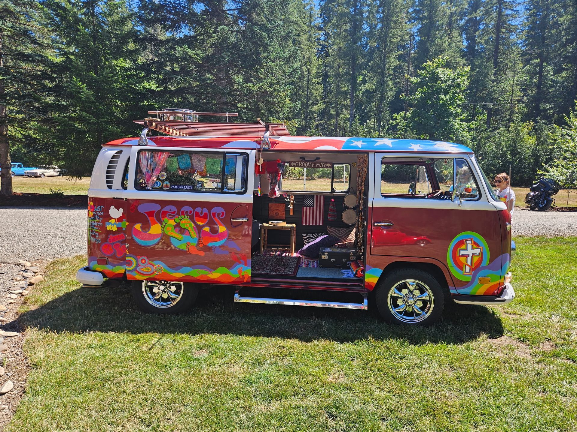 Colorful, painted van with open door parked on grass, in front of trees.