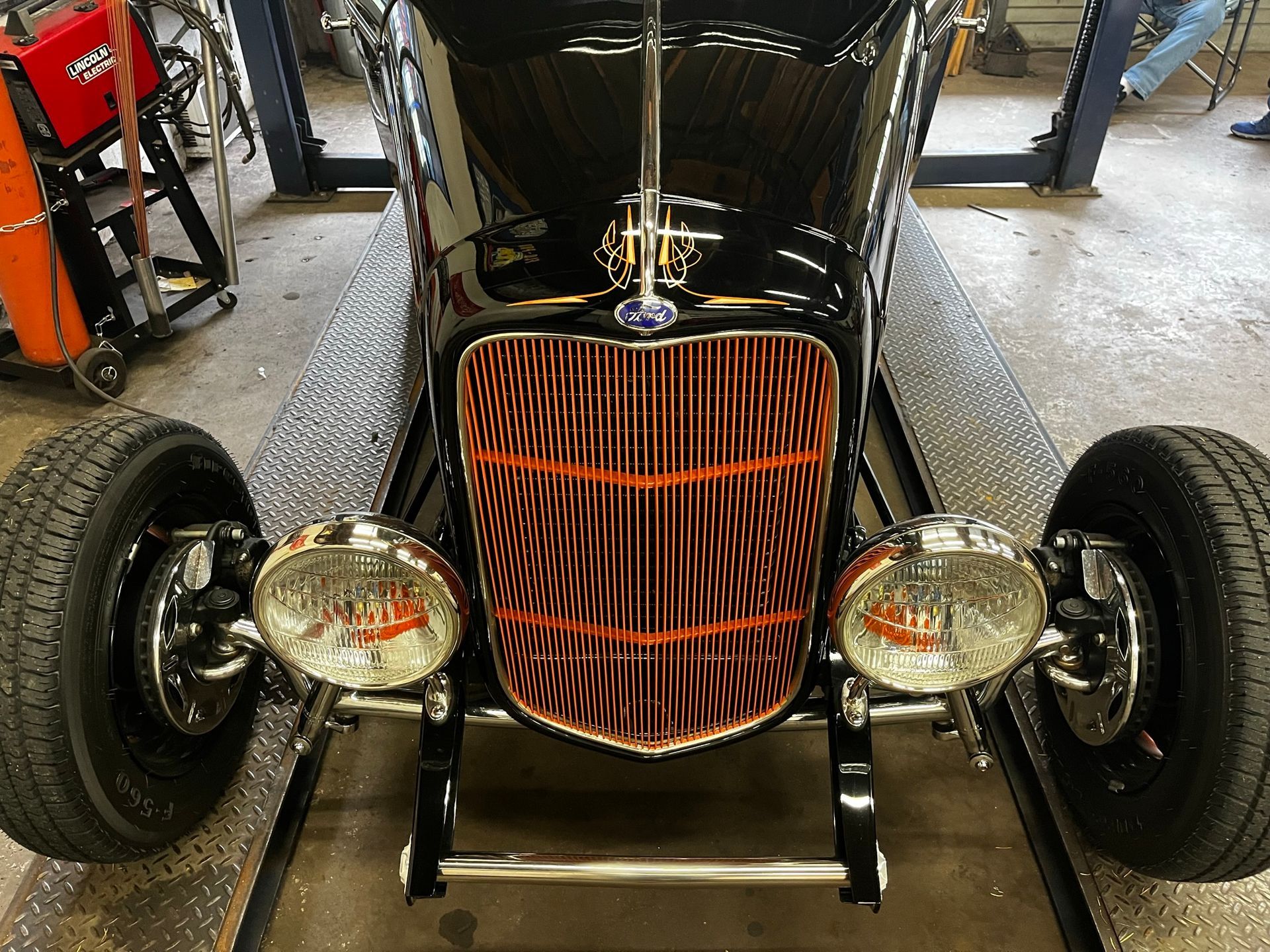 Black classic car, front view, shiny grill with copper accents, round headlights, in garage.
