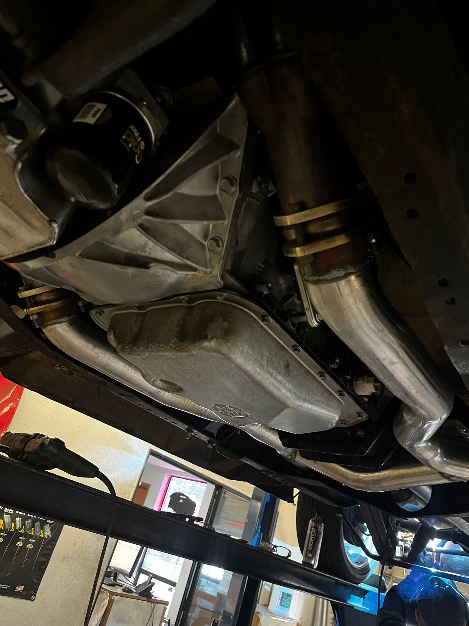 Underside of a vehicle, showing engine components including a silver oil pan, headers, and transmission.