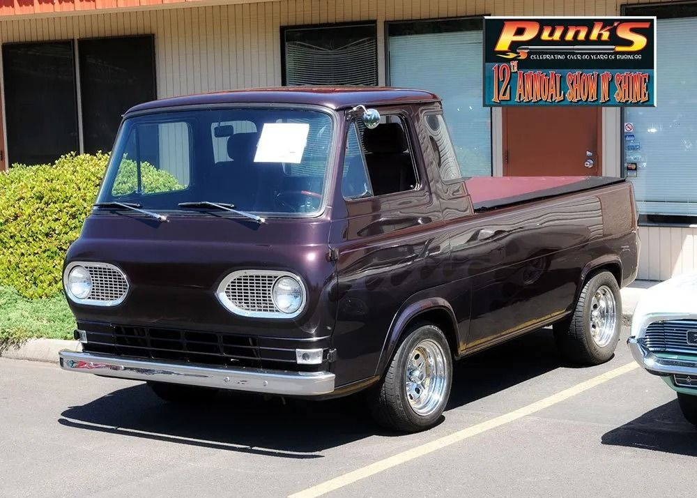 Dark purple 1960s Ford Econoline pickup truck parked in front of a building.