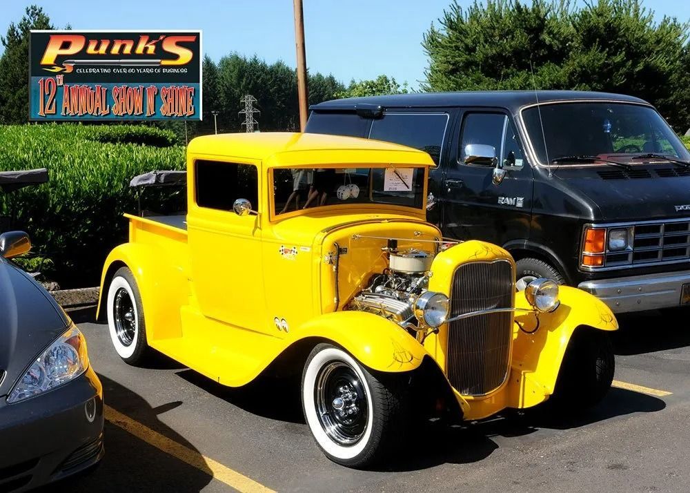 Yellow classic truck parked near a black van, in front of a restaurant sign.