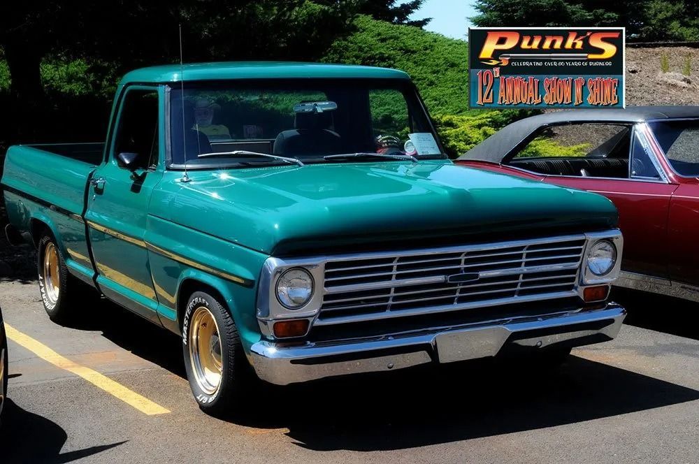 Green vintage pickup truck with gold wheels parked in a lot, sunny day.