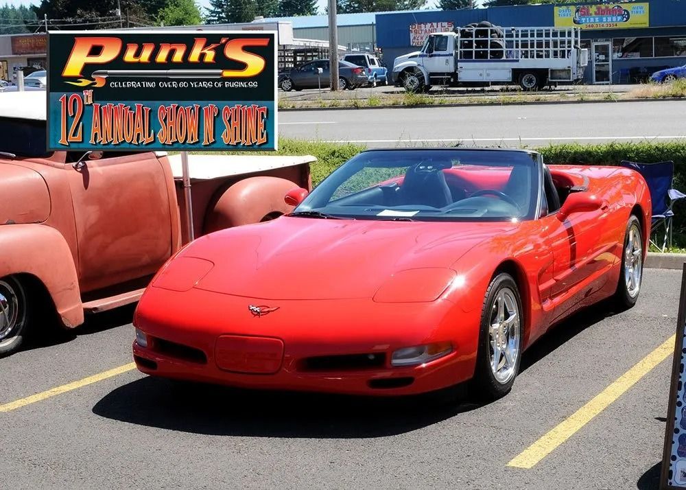Red convertible Corvette at a car show, parked next to an older rusty pickup truck.