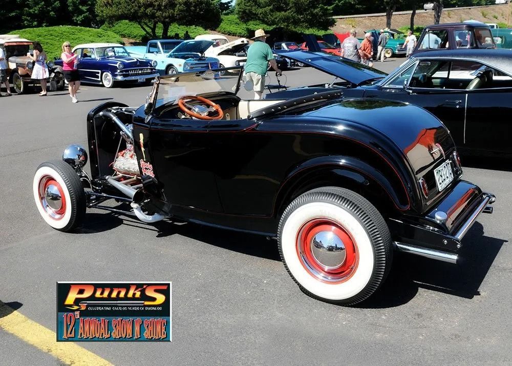 Black hot rod roadster with white-walled tires at a car show.