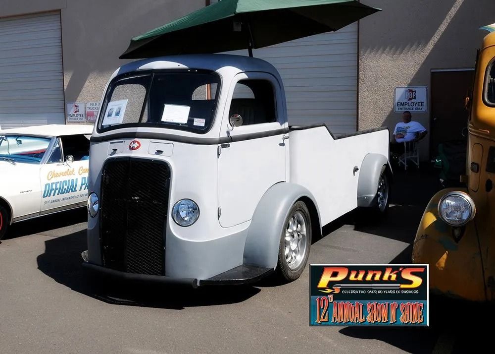 Gray and white vintage pickup truck with umbrella on display at car show.