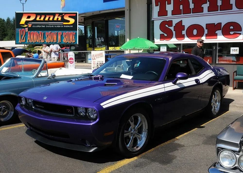 Purple Dodge Challenger with white racing stripes parked outside a thrift store.