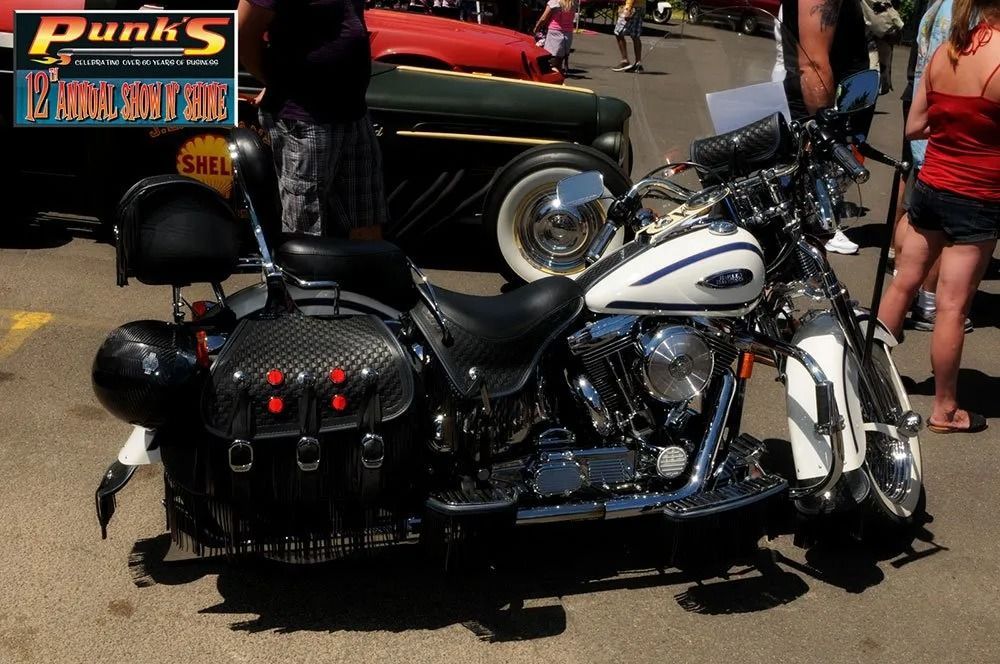 White and chrome Harley-Davidson motorcycle with black saddlebags, parked outdoors at an event.