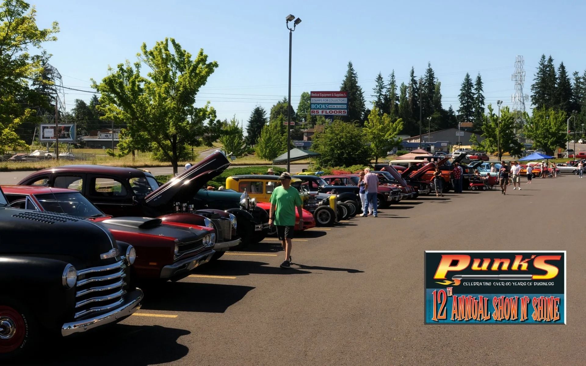 Classic cars parked at an outdoor event on a sunny day. People are walking around and looking at the cars.