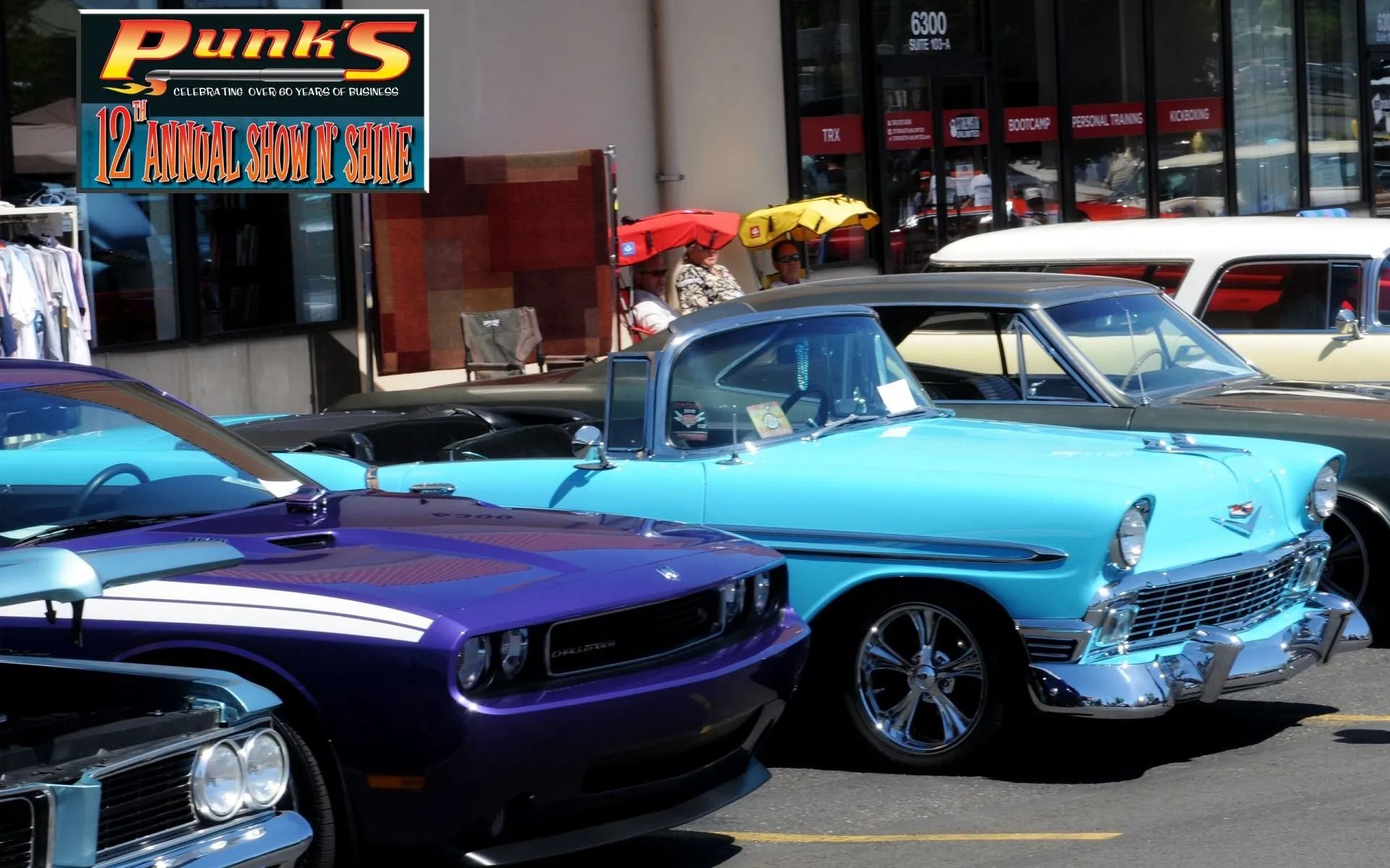 Classic and modern cars displayed outdoors; purple Challenger and turquoise convertible are prominent.