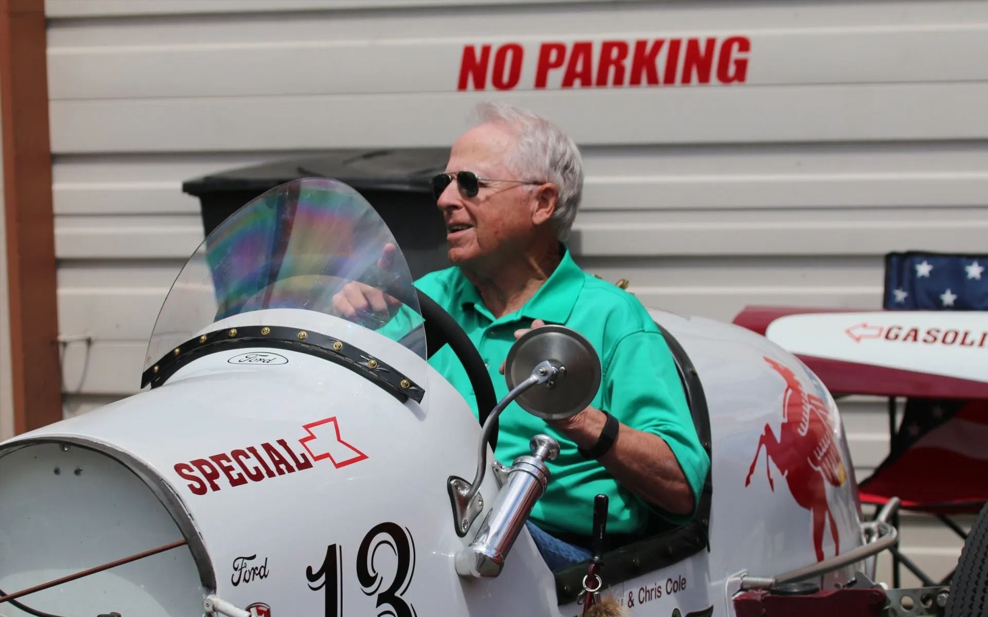 Man driving a white racing car with red accents; 