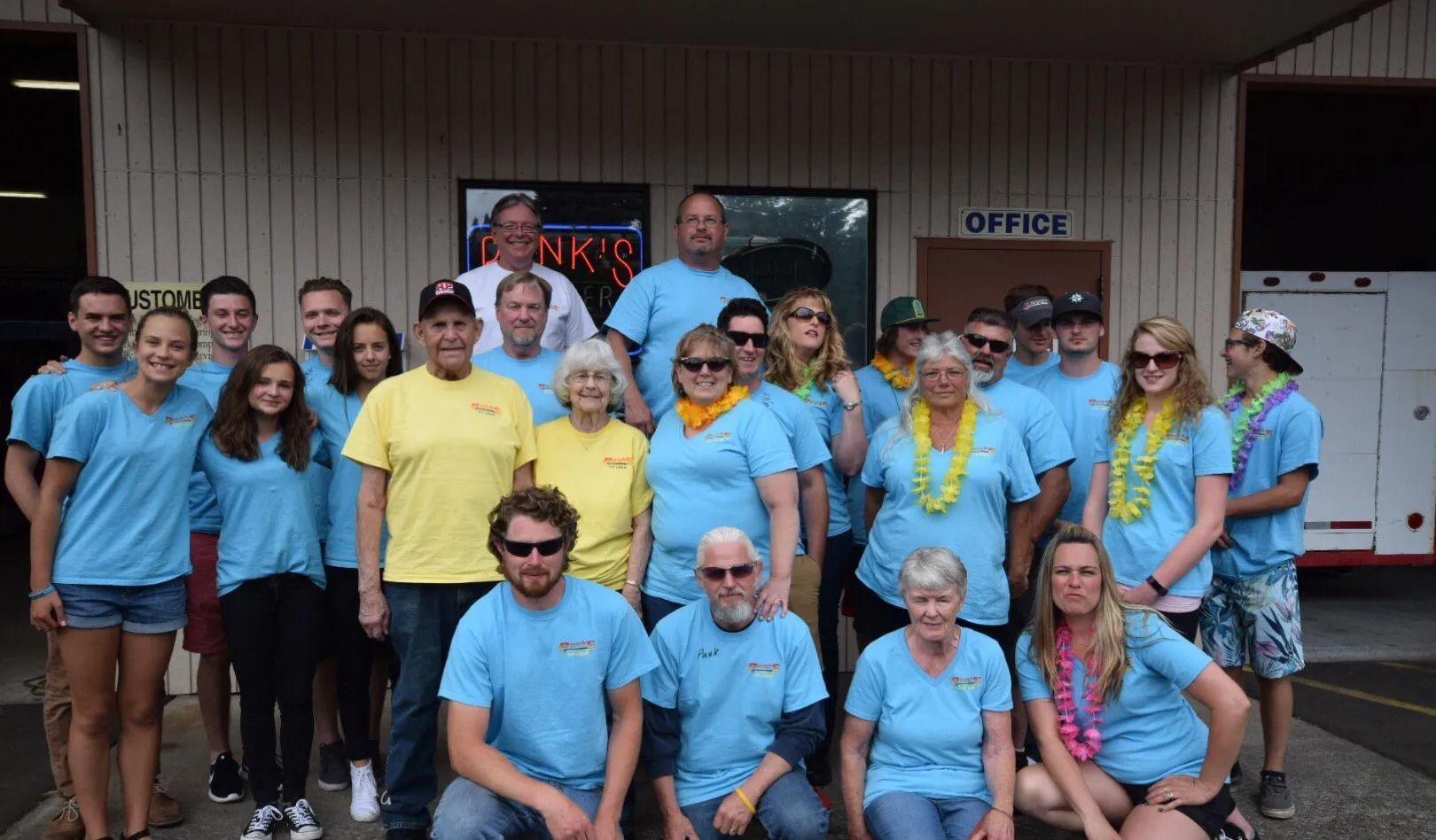 Group of people in matching blue shirts pose in front of a building. Some wear leis. 