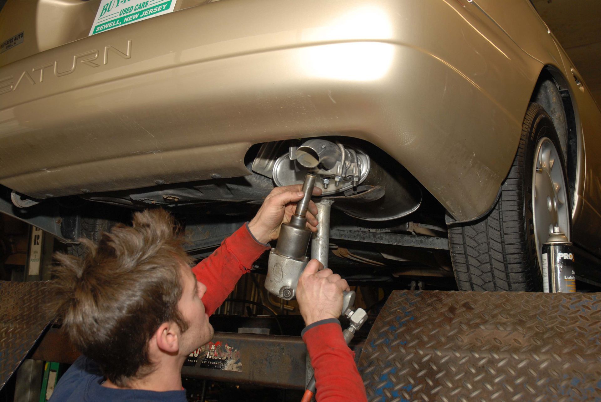 Mechanic working on car's exhaust system, using a wrench while the car is on a lift.