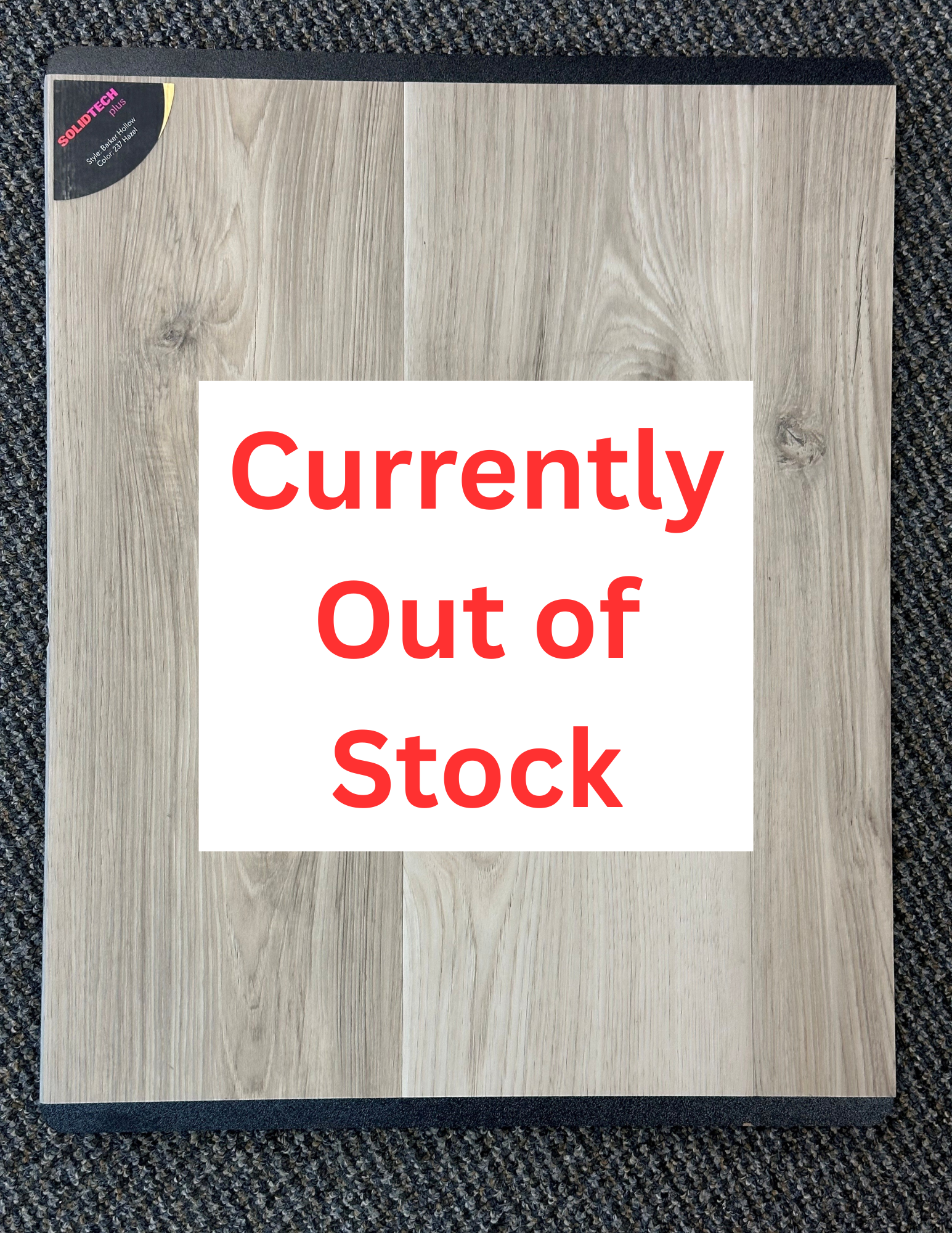 Light-brown wood flooring sample, close-up view. Displayed on a dark gray carpeted surface.