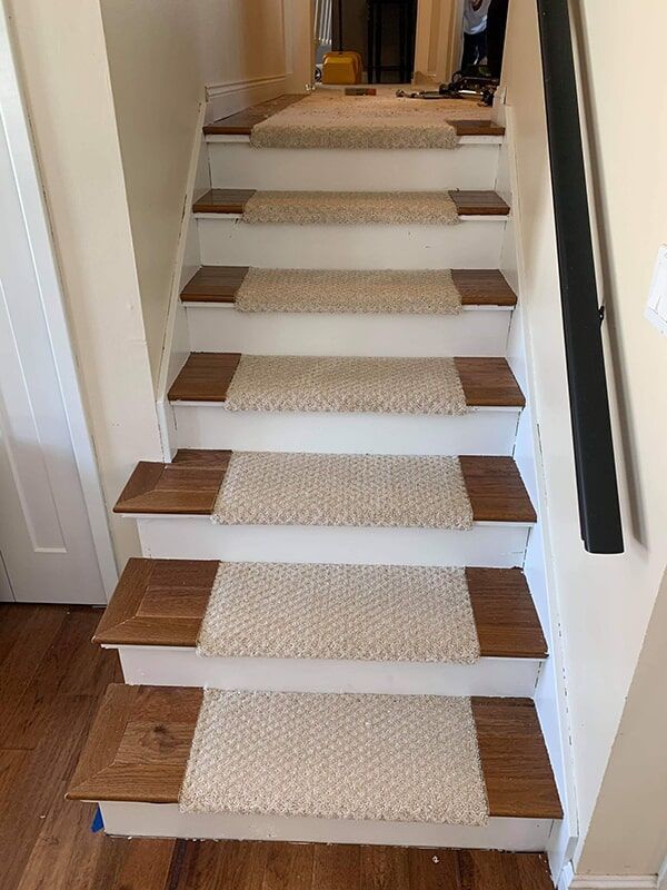 Two workers installing gray carpet tiles in an empty room. One kneels, while another is on the floor with tools.