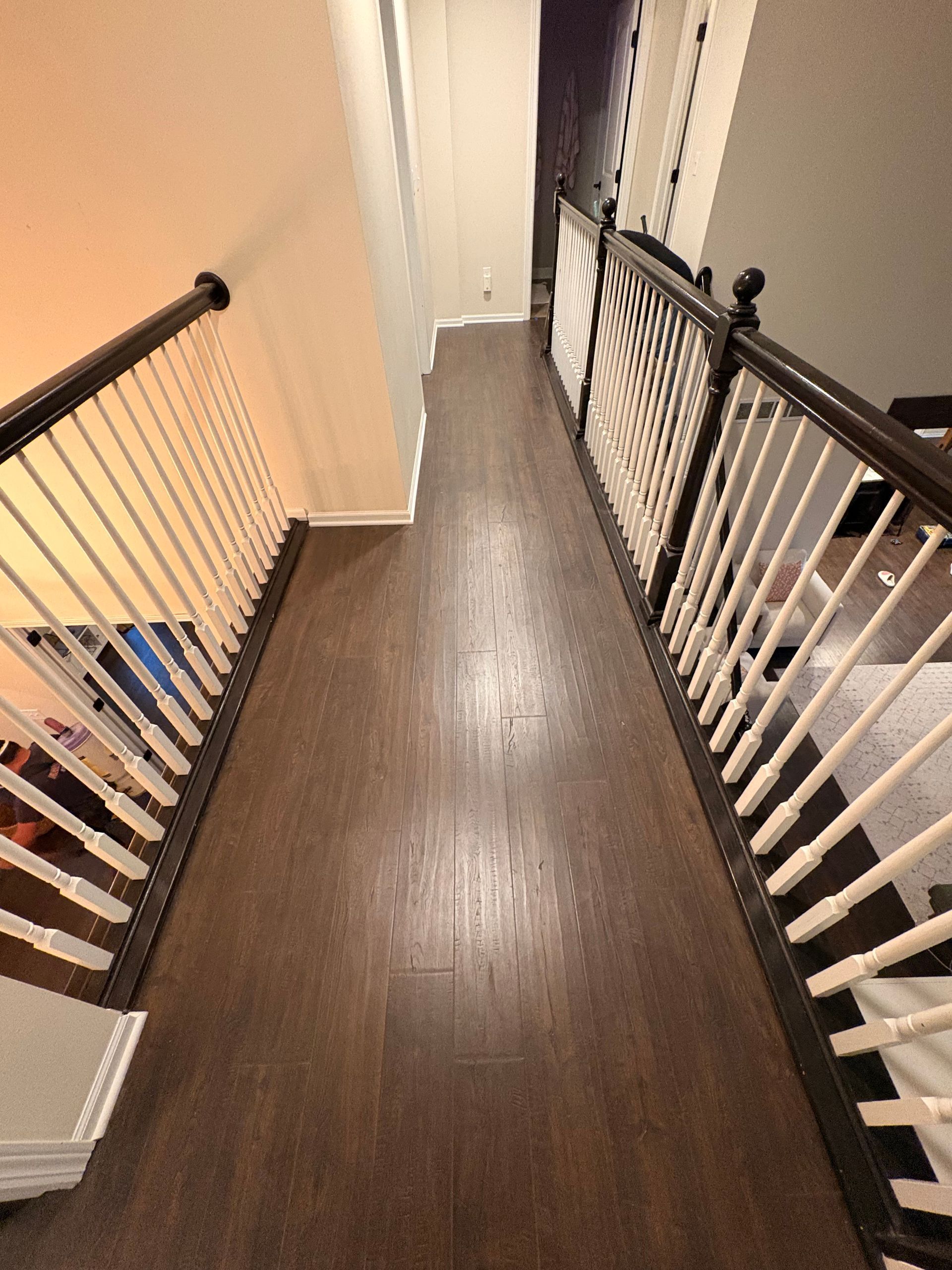 Overhead view of a hallway with brown hardwood floors, white banisters, and dark wooden handrails.