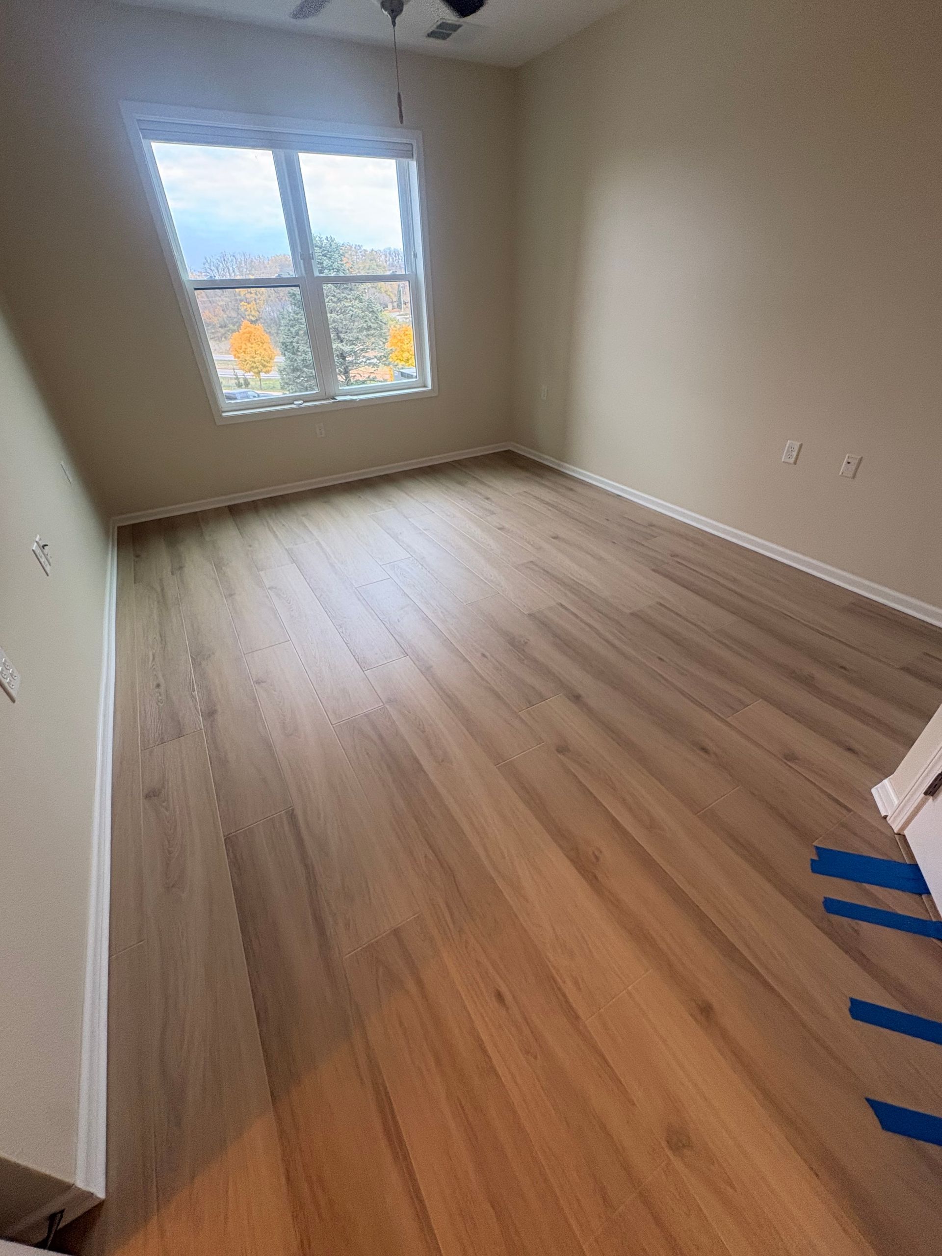 Empty room with wood-look flooring, a window, and beige walls.