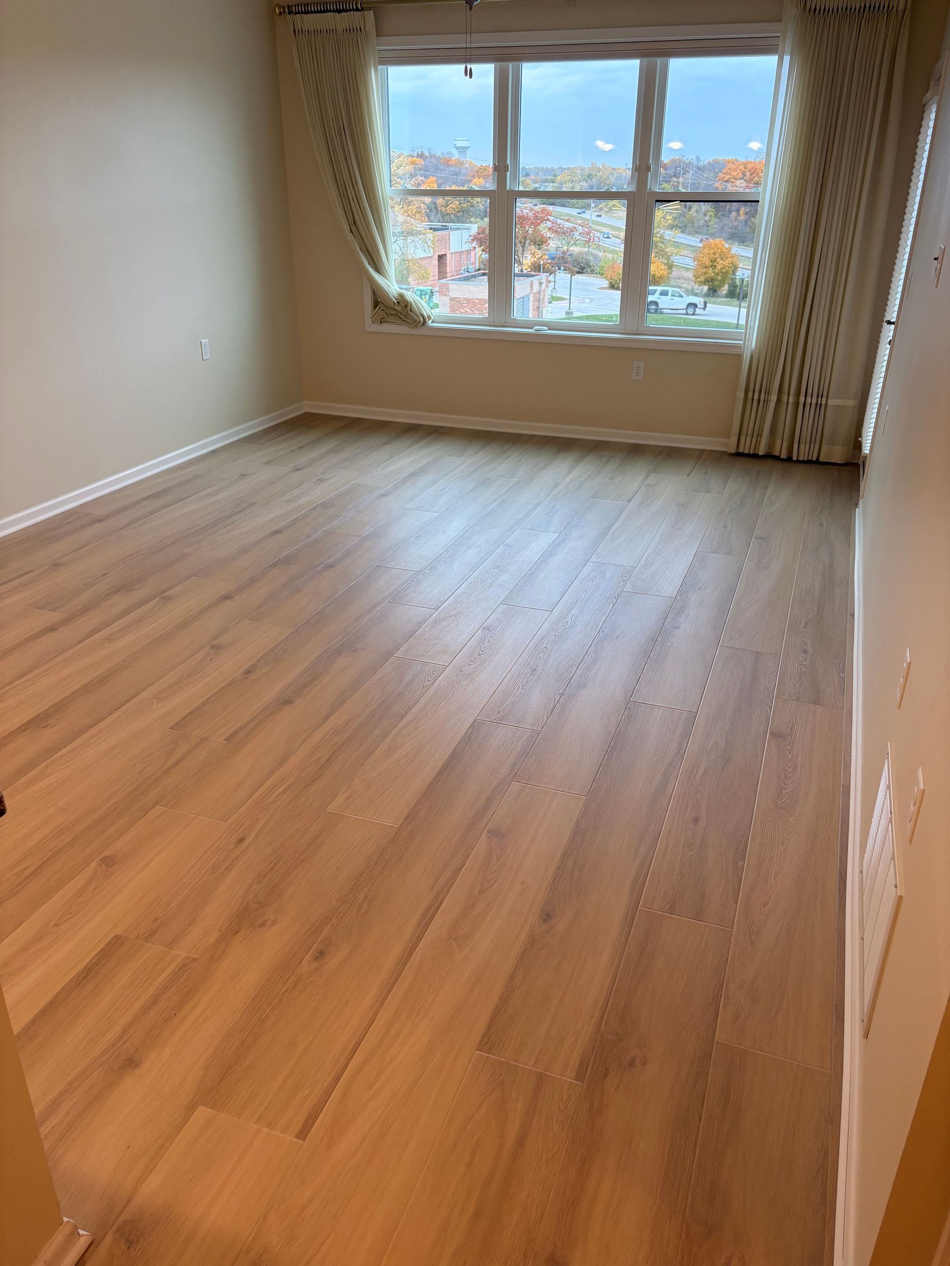 Empty room with light wood-look flooring, beige walls, and a window with a city view.