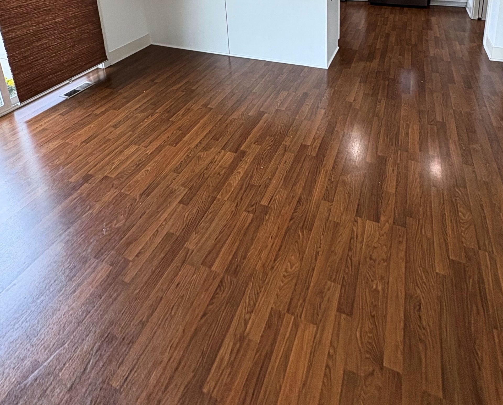 Wood-look laminate flooring in a room with a wall and window with a blind.