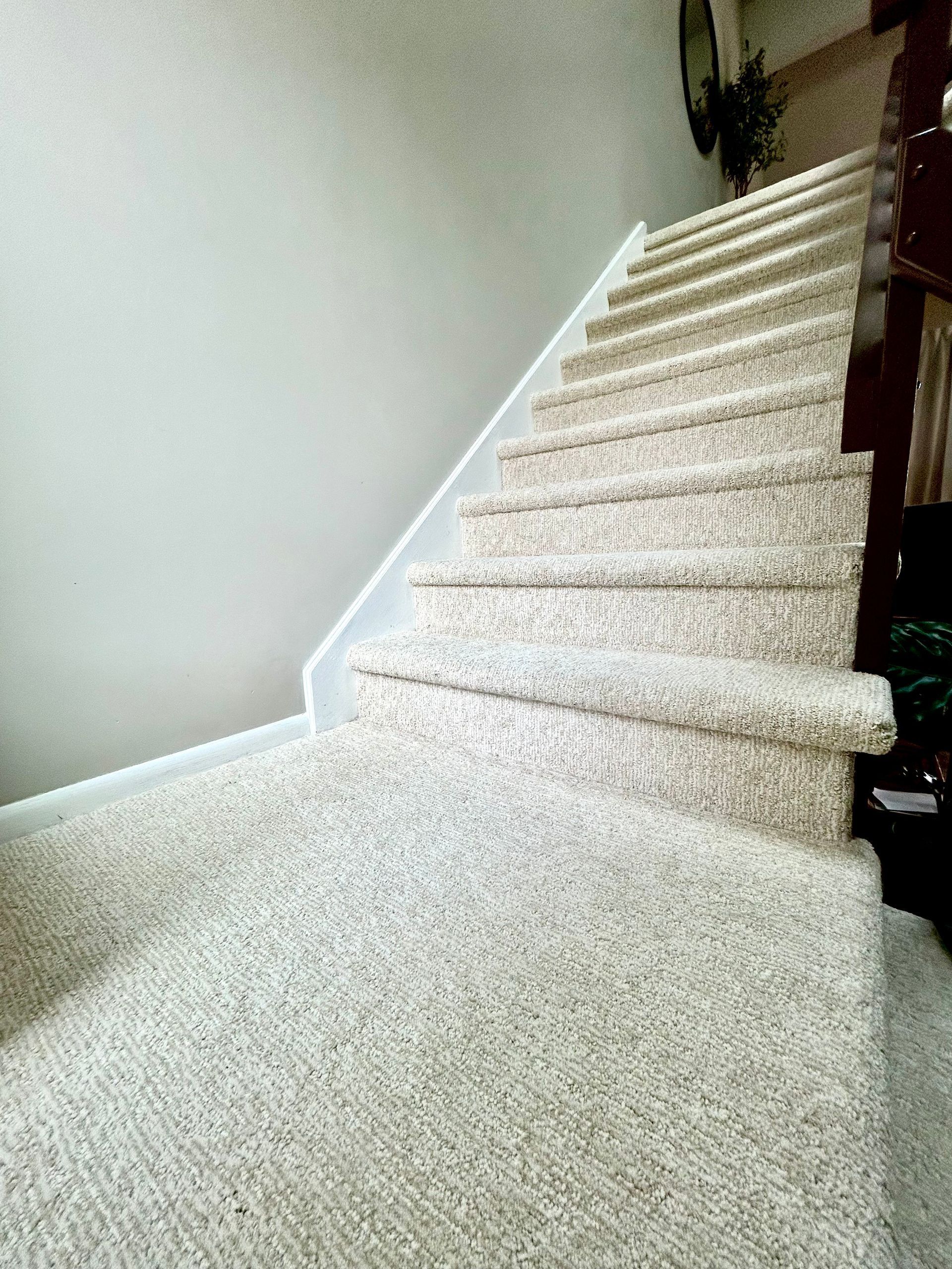 Kitchen backsplash with gray rectangular tiles being installed between white cabinets. A bucket of tile adhesive and tools are visible.