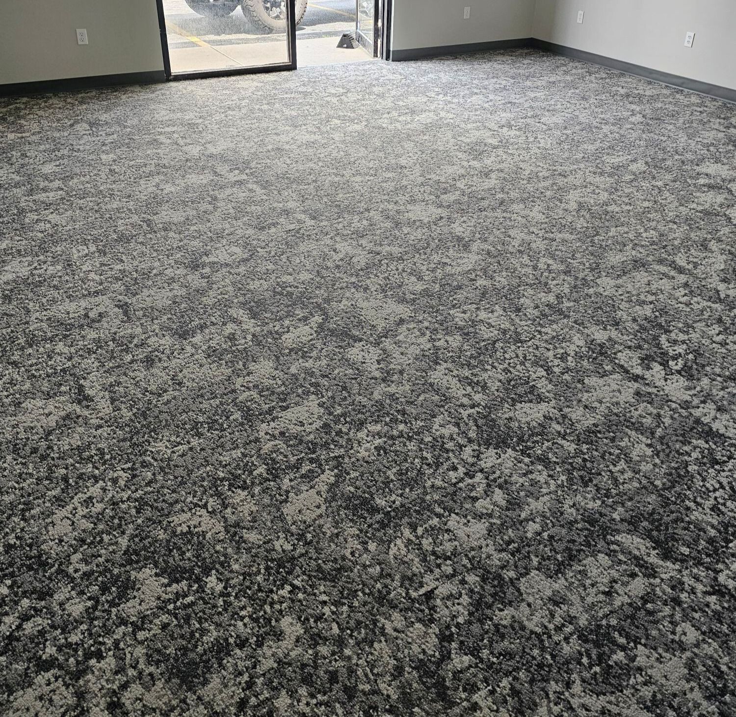 Inside of a tiled shower stall featuring white rectangular tiles on the floor and marble-like tiles on the walls, with a drain in the floor center.