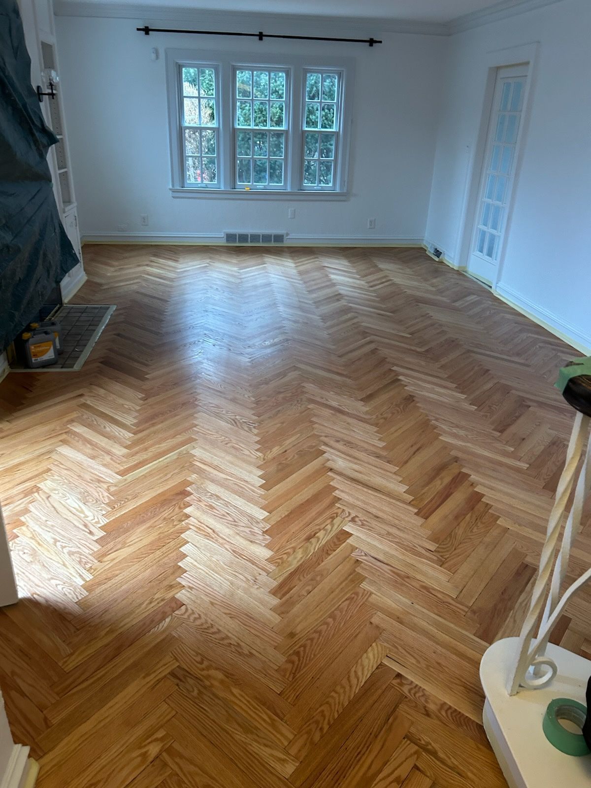 Hardwood floors lead to a carpeted staircase. The staircase has a wooden banister and is wrapped in plastic for protection.