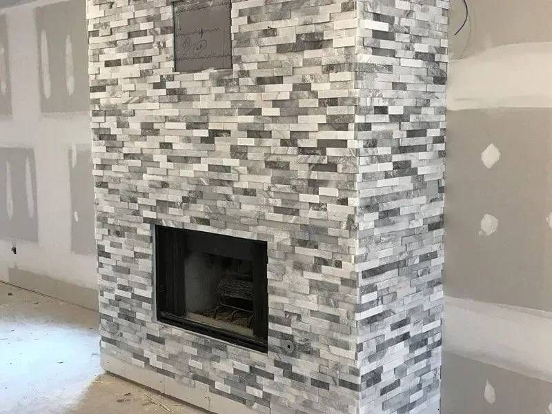 Fireplace with gray and white stone tile surround; a built-in fireplace with a black framed opening is centered.