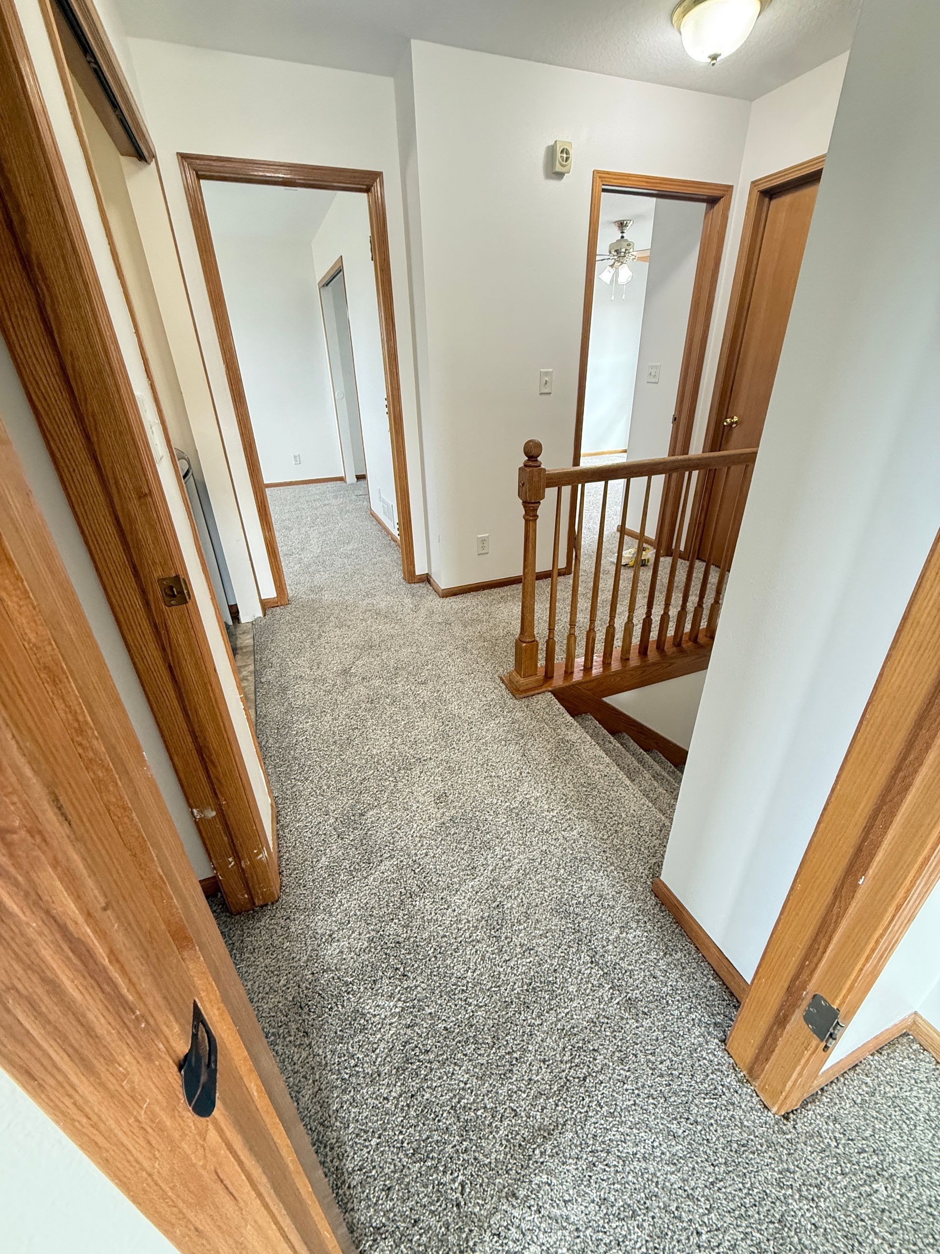Hallway with gray carpet, white walls, and wood doors leading to rooms and staircase. 