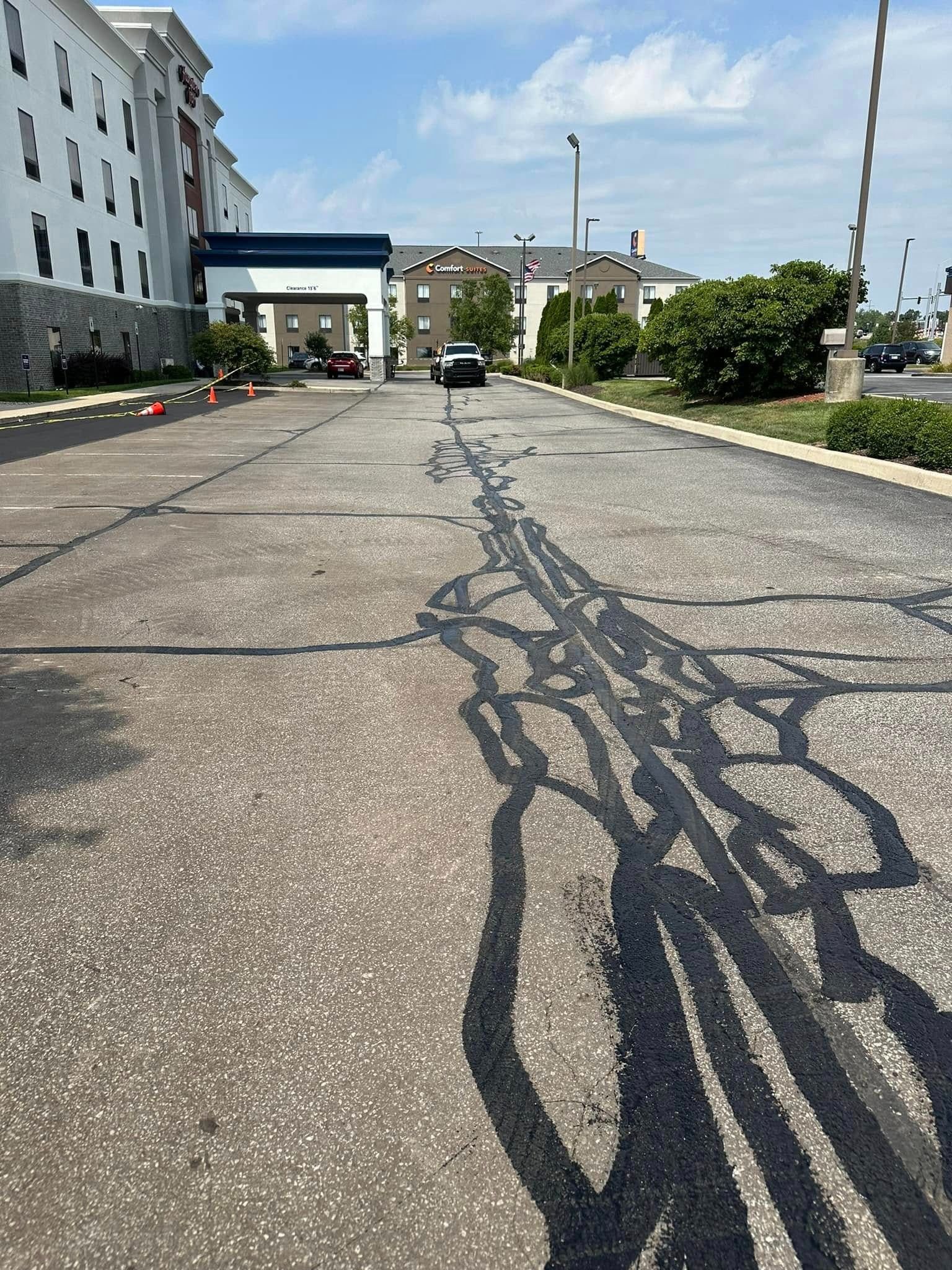 Asphalt driveway with recent black sealant repairs; Hampton Inn hotel in background.