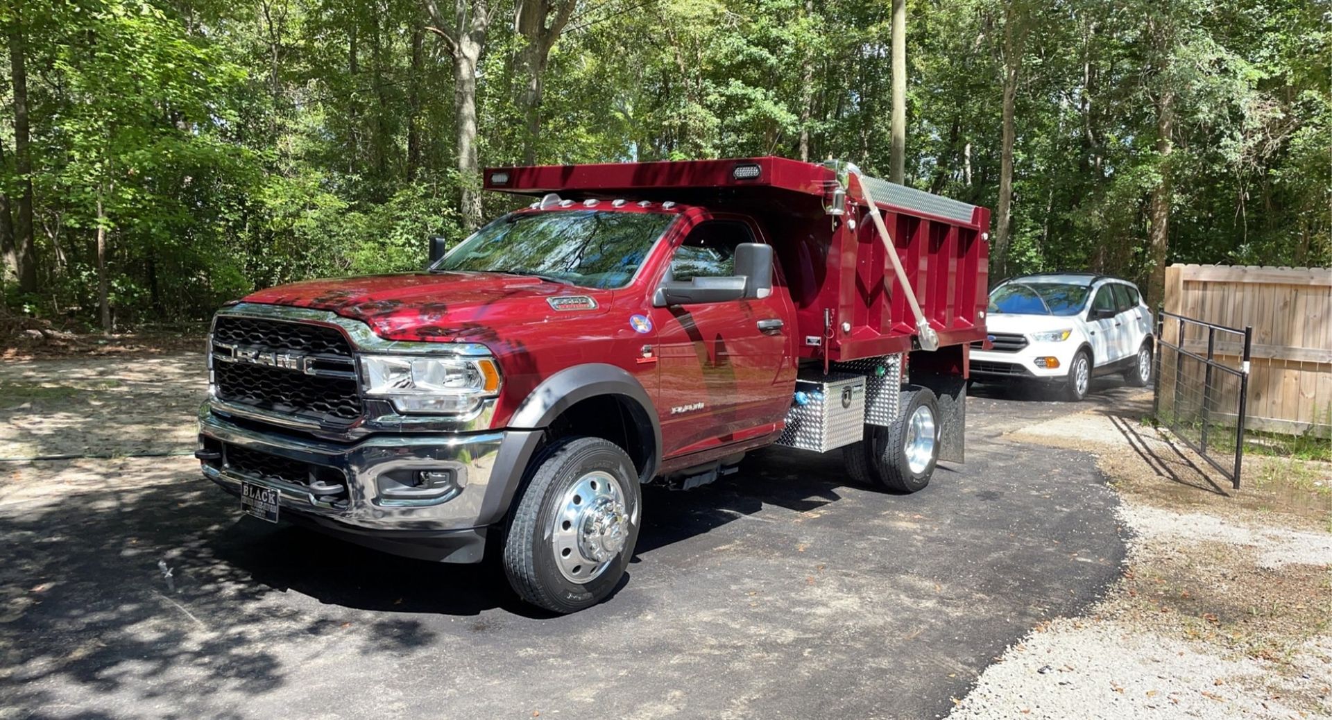 Red dump truck parked on a driveway with a white SUV in the background, trees visible.