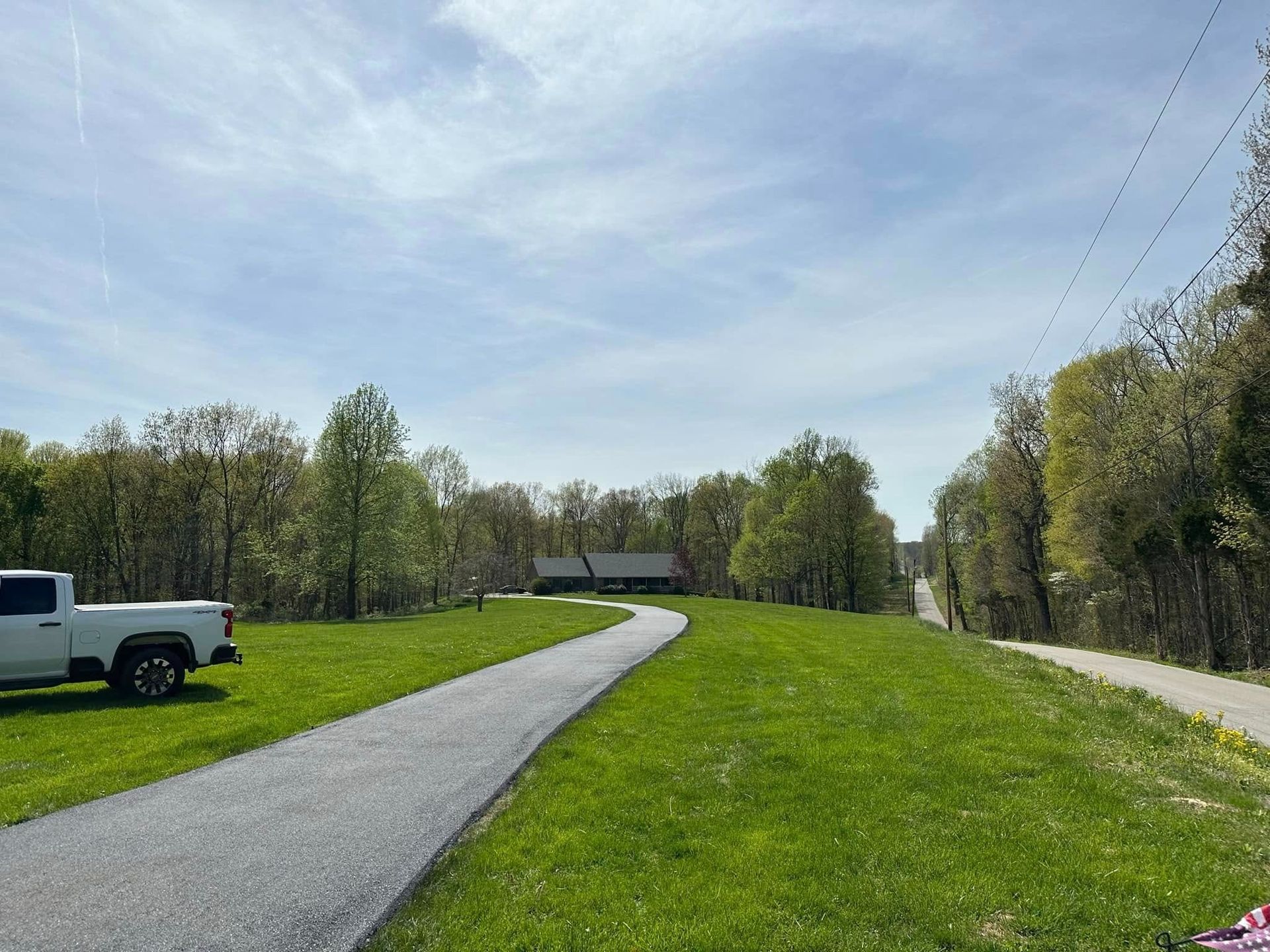 A gravel path leads uphill towards a building surrounded by trees under a cloudy sky. A white truck is on the left.