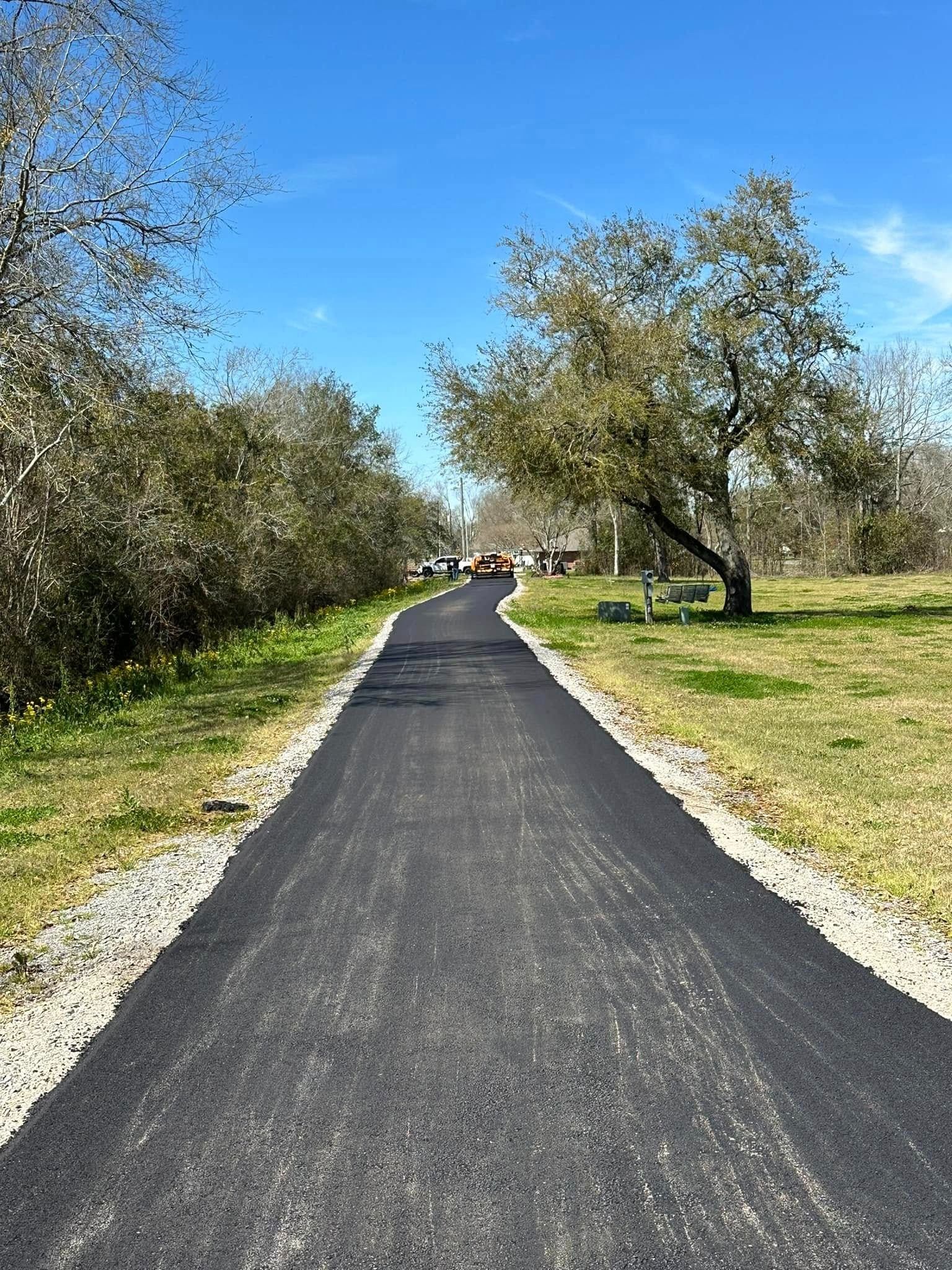 Paved path through a park, with trees on either side and blue sky above.