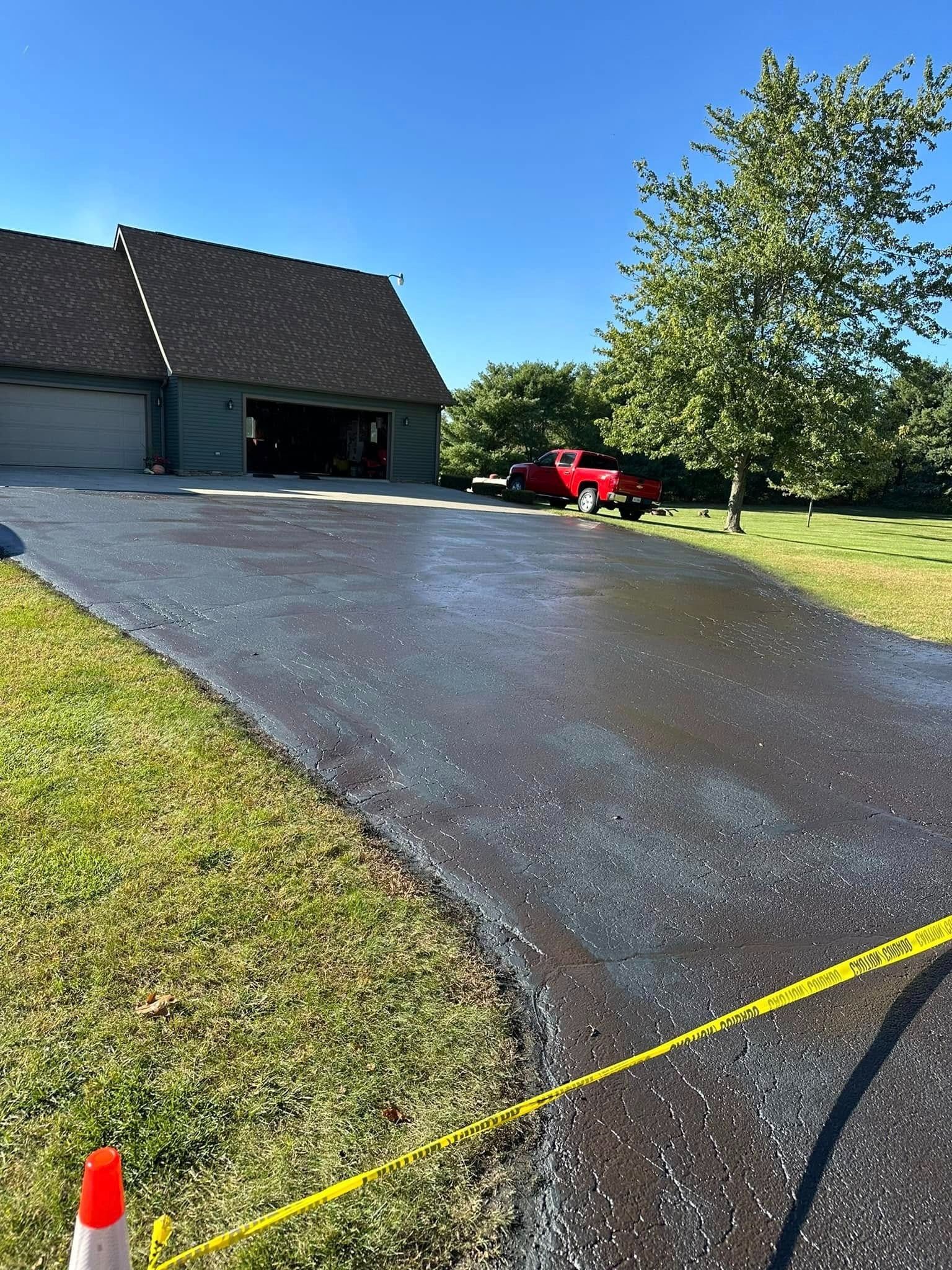 Newly sealed asphalt driveway in front of a house and garage with a red truck in the distance.