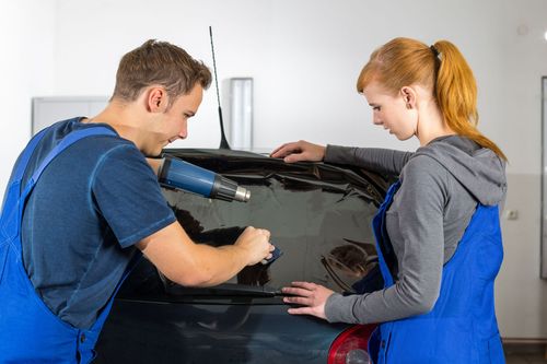 Two mechanics working on a car windshield in a garage