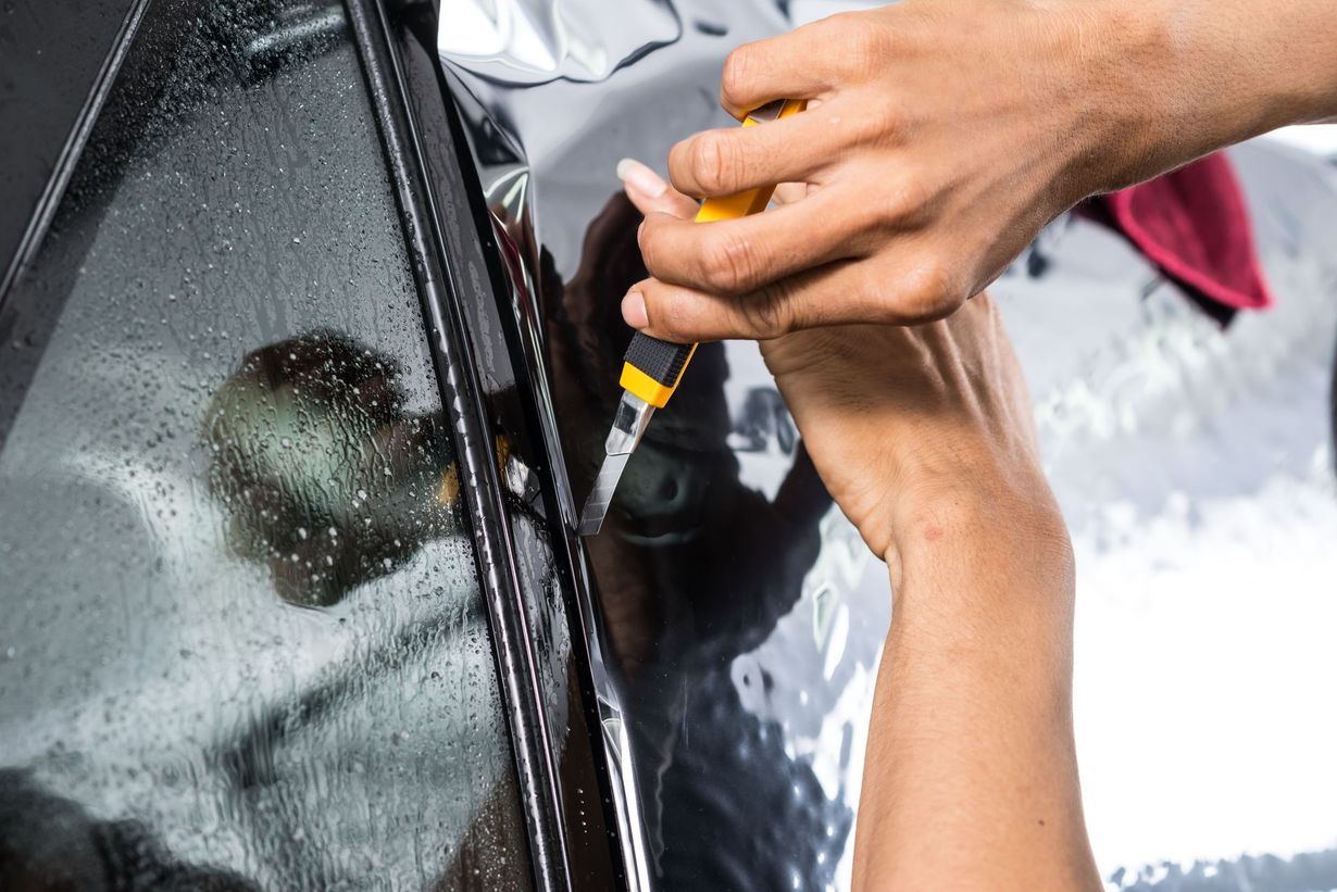 Hands polishing a black car window with a yellow tool outdoors