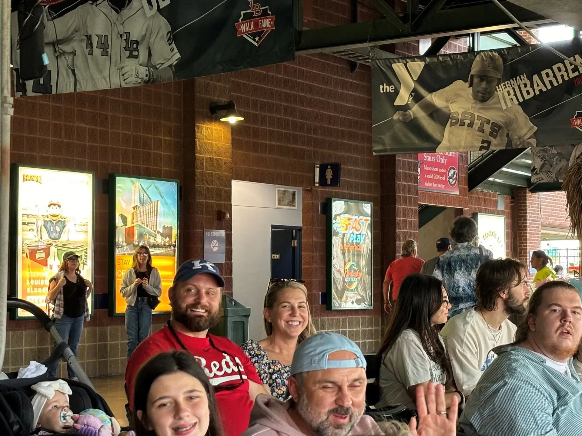 People gathered at a baseball stadium.  Smiling faces, stadium décor.  Daylight.