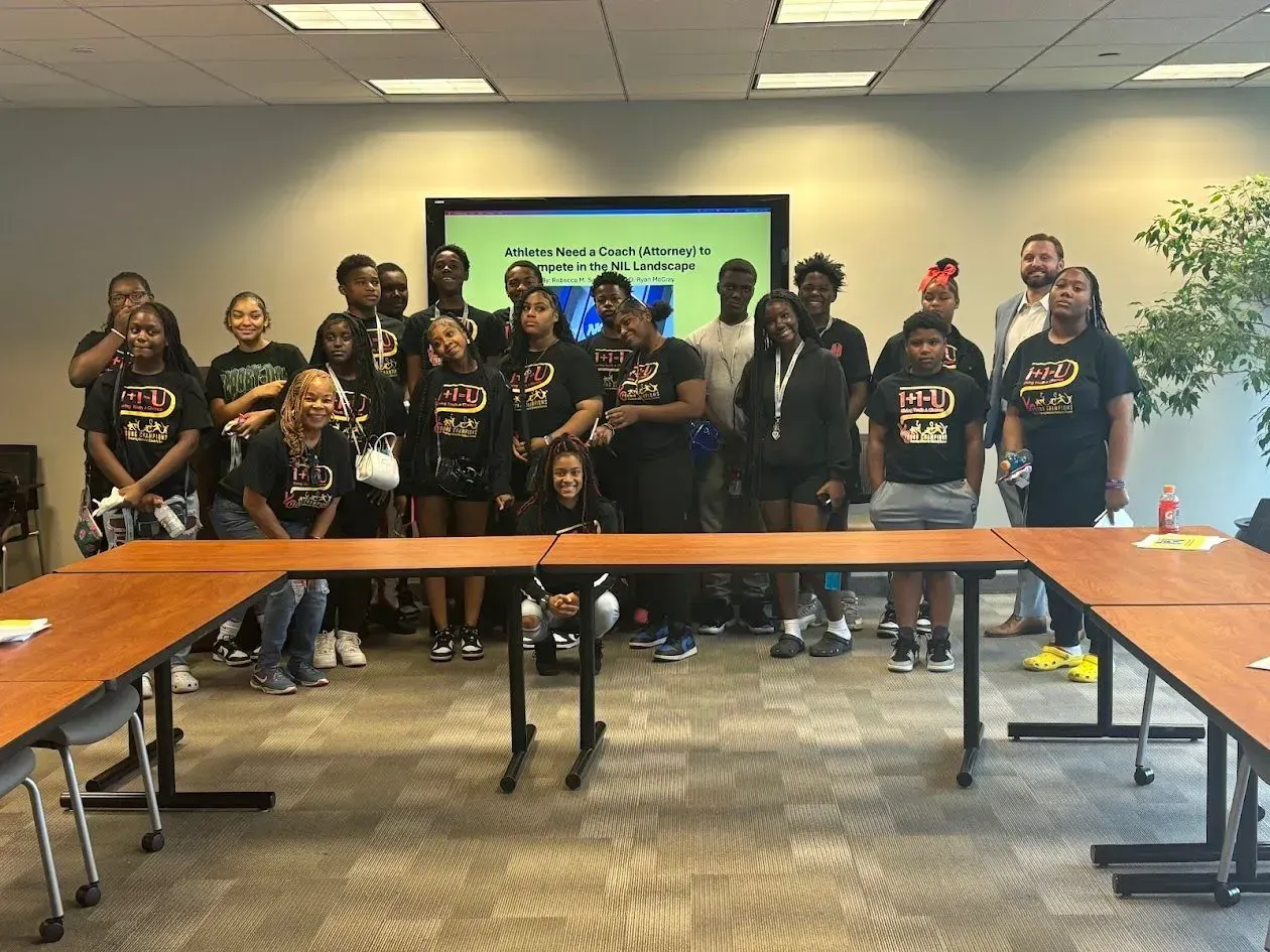 A group of young people wearing black shirts with gold lettering stand in a meeting room.
